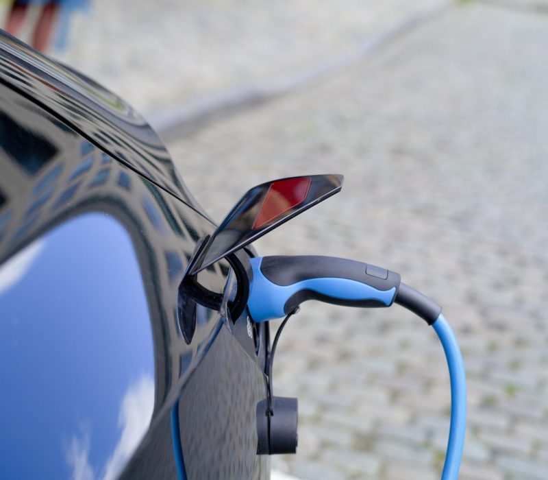 Electric car charging with reflection on shiny blue surface on cobblestone street.